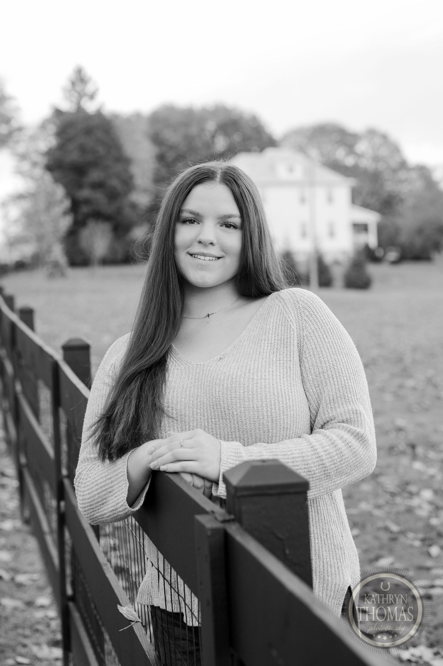 Black and white portrait by wooden fence with classic farmhouse in background.