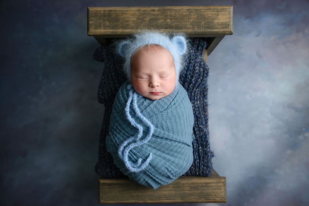 Newborn sleeping peacefully in gray wrap on wooden crate with soft atmospheric lighting.