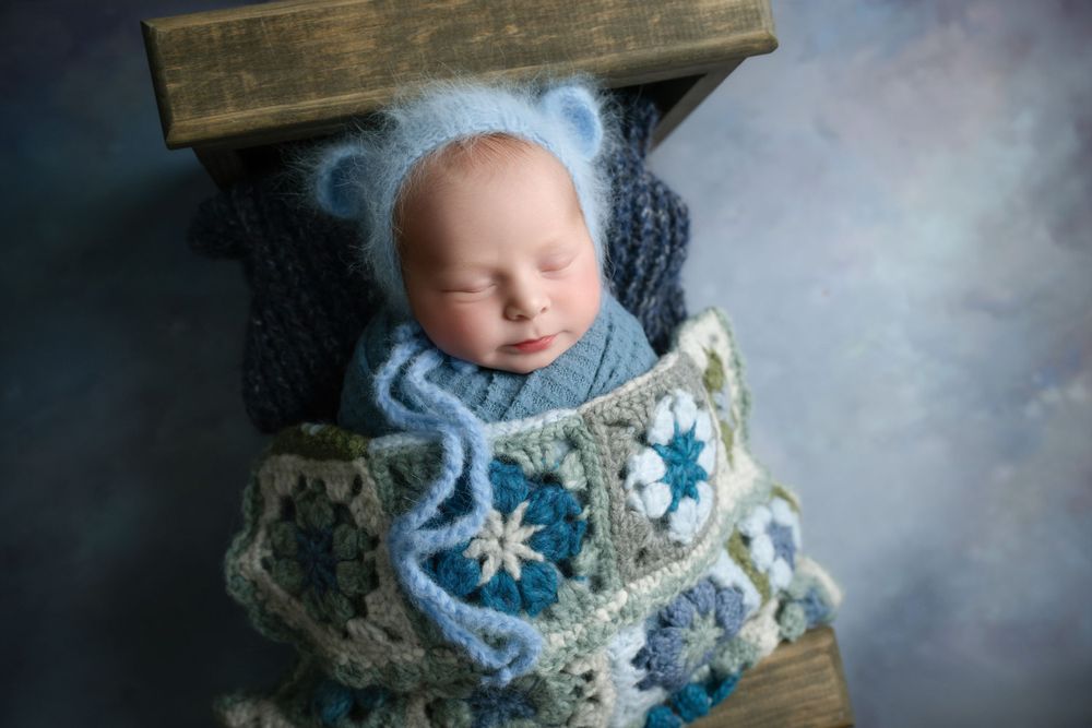 Sleeping baby in blue wrap nestled in vintage wooden crate with patterned blanket.