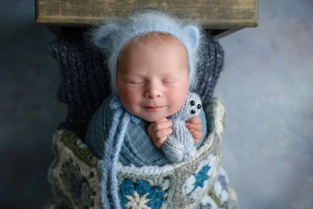 Sleeping baby in blue wrap on wooden surface with decorative floral blanket.