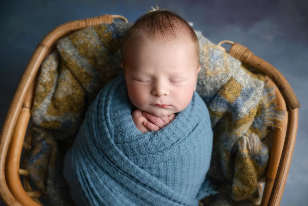 Peaceful sleeping newborn wrapped in blue knit blanket lying in wicker basket.