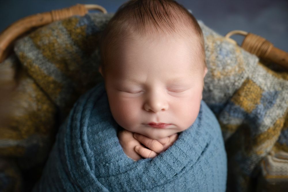Peaceful newborn sleeping in blue knit wrap on textured blanket.