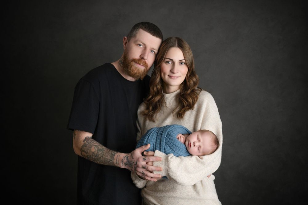 Studio family portrait with parents in casual wear holding their newborn.