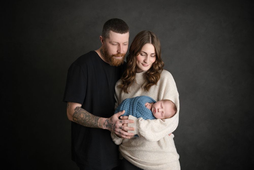 Intimate family portrait with parents gazing at their wrapped newborn.