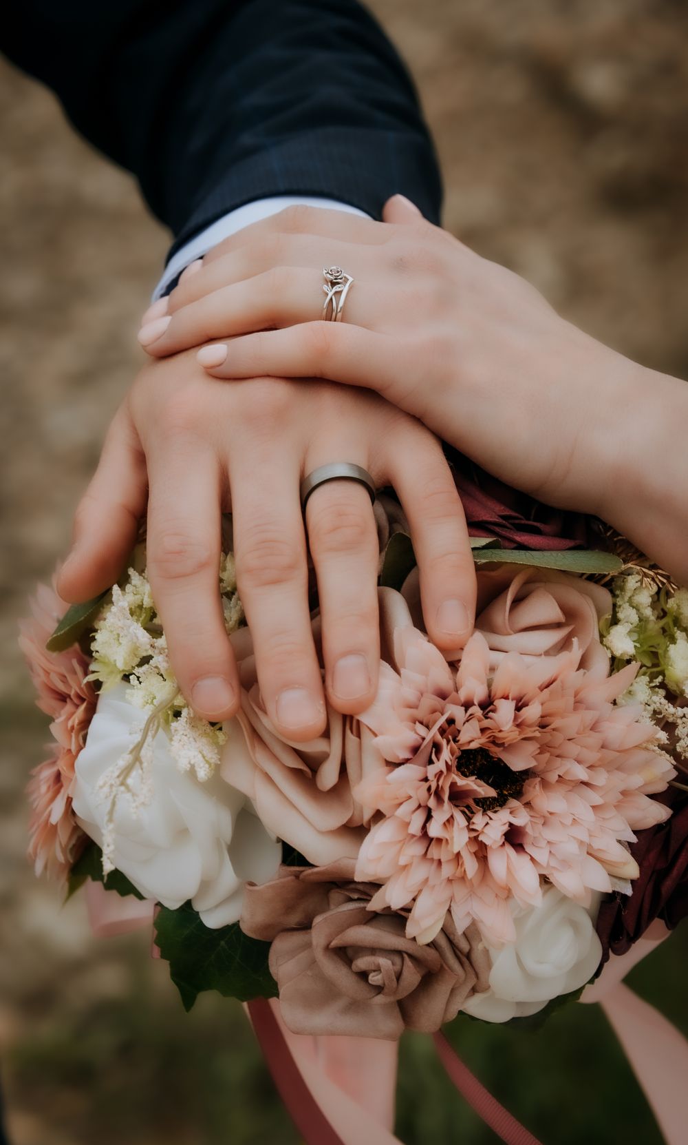 Close-up shot of wedding rings and hands resting on a bouquet of pink and white flowers.
