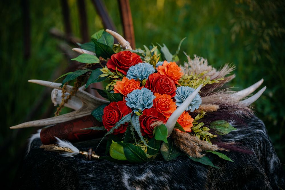 Colorful floral arrangement with red and orange roses mixed with pale blue flowers against a dark background.