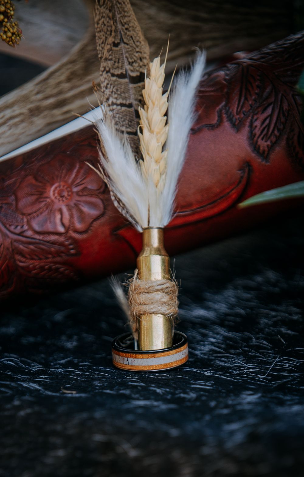 Decorative wheat stalk boutonniere wrapped in twine with gold accents against leather background.