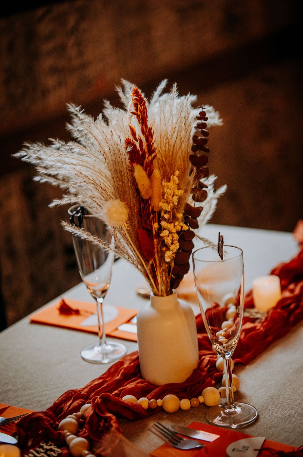 Bohemian table setting with cream-colored vase holding dried pampas grass and burgundy accents.