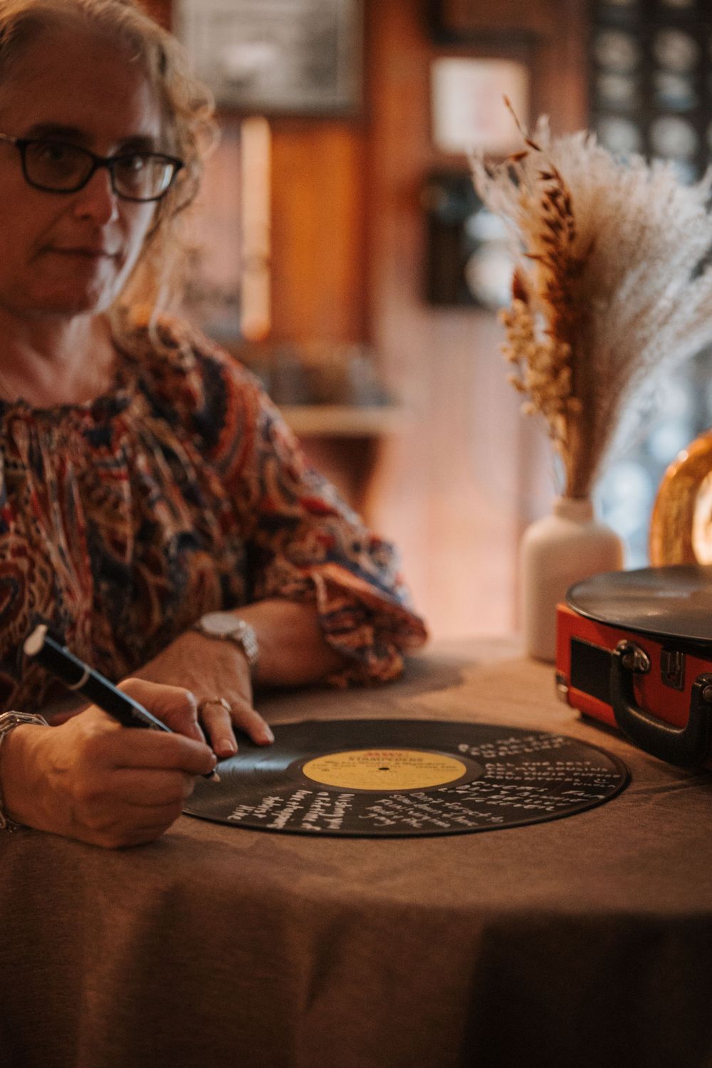 Vinyl record being signed as a wedding guest book with dried floral decorations nearby.