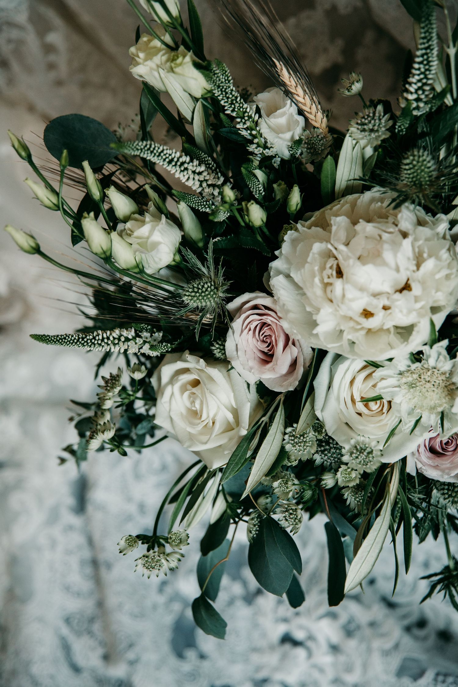 Elegant white and blush rose bouquet with eucalyptus leaves and delicate greenery against textured background.