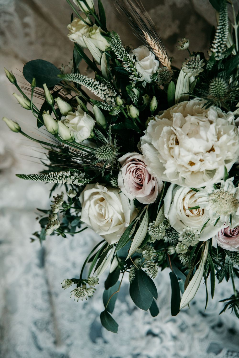 Elegant white and blush rose bouquet with eucalyptus leaves and delicate greenery against textured background.