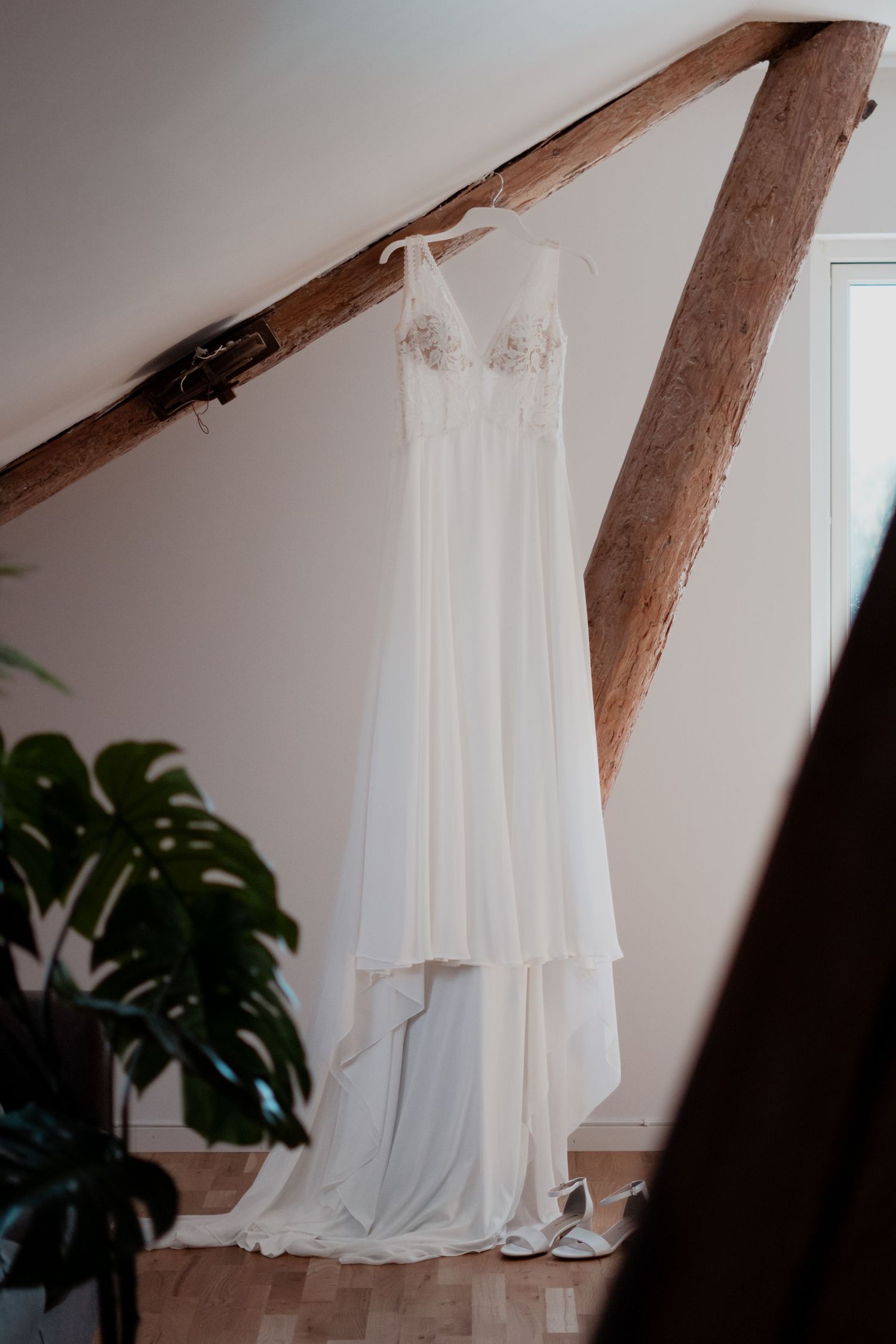 White wedding dress hanging from rustic wooden beams in a bright interior space.