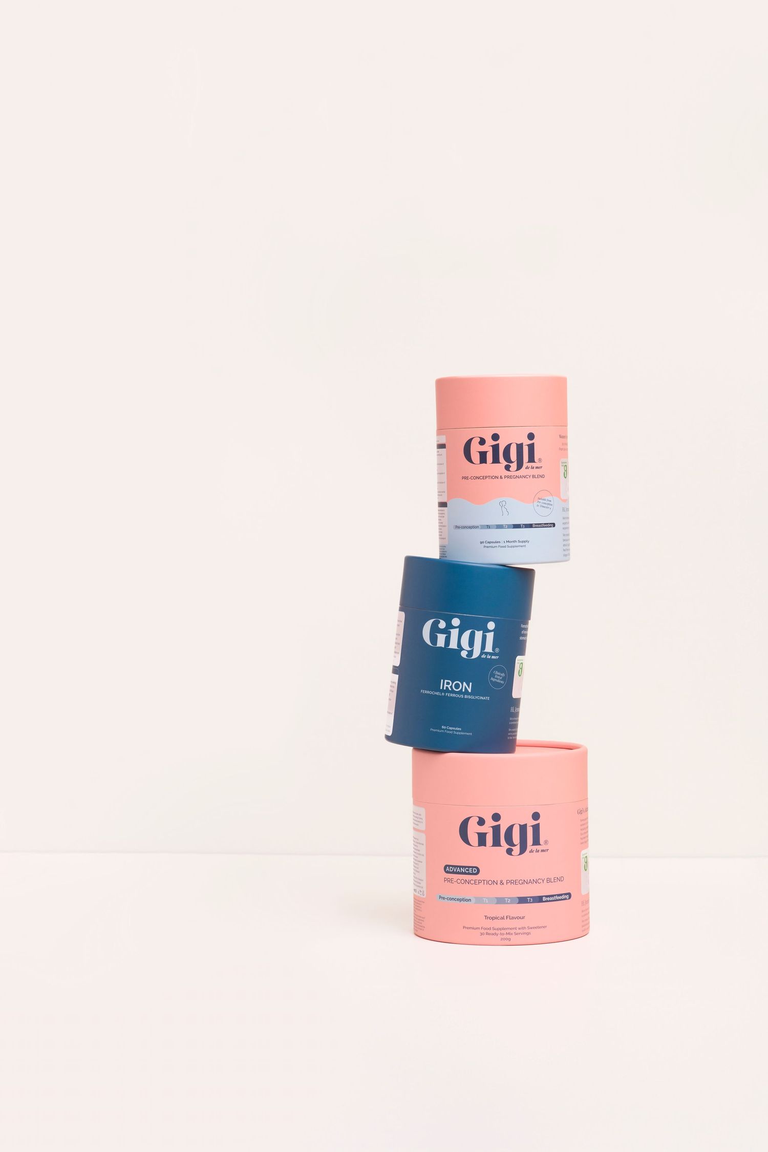 Hand reaching for Gigi supplement drink sachet out of the packet. Pink backdrop. There is a pre made drink in front.