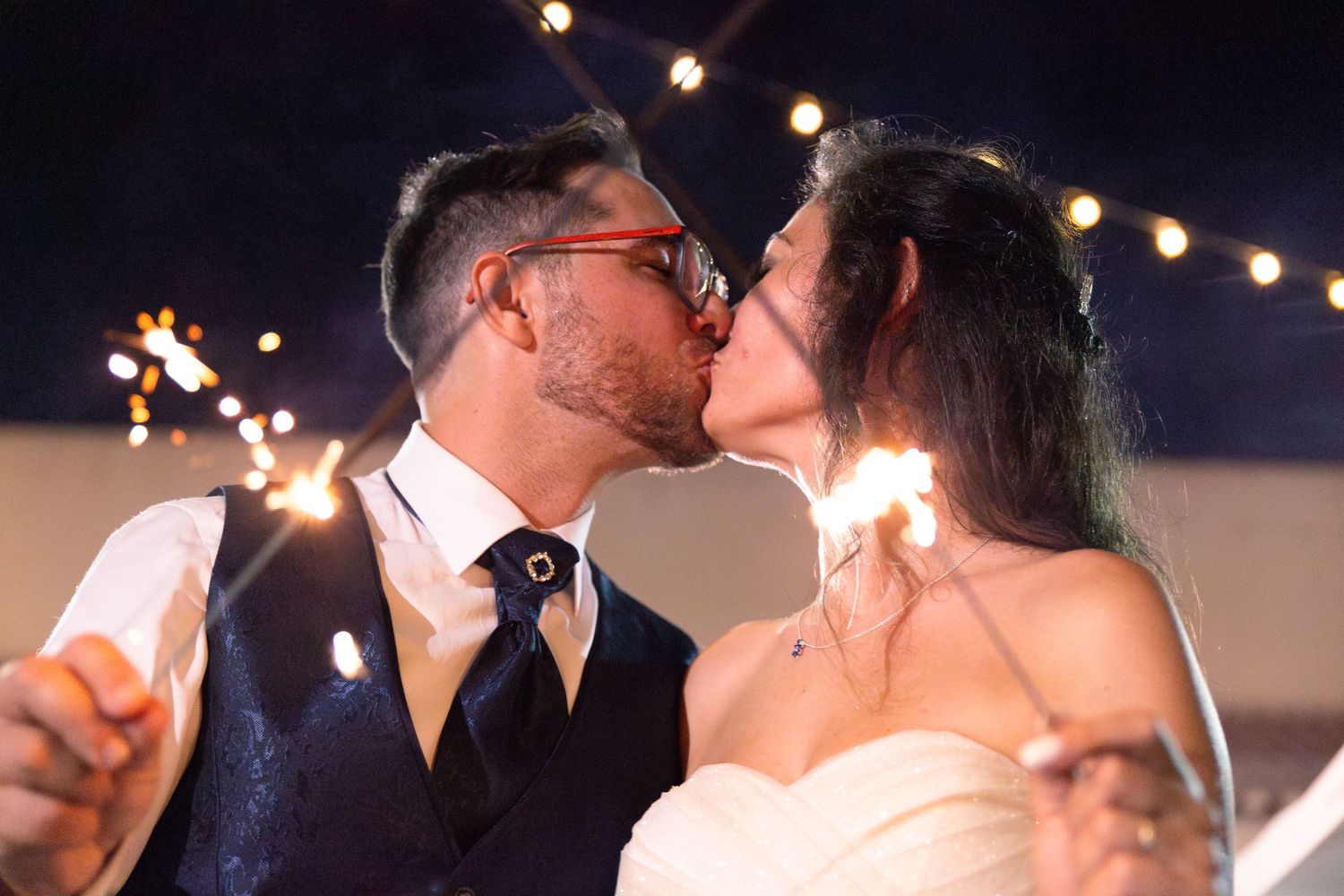 A romantic sparkler kiss between newlyweds during their evening wedding celebration.