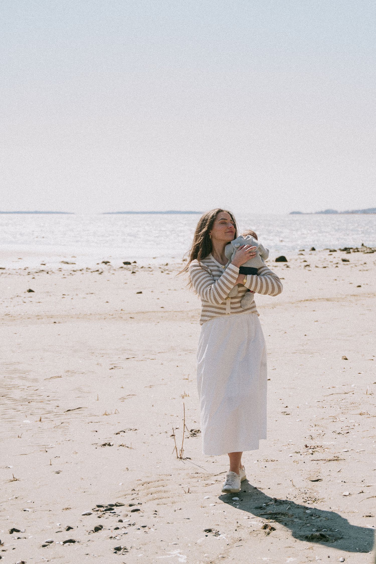 New mom holding newborn during lifestyle photo session at RI beach