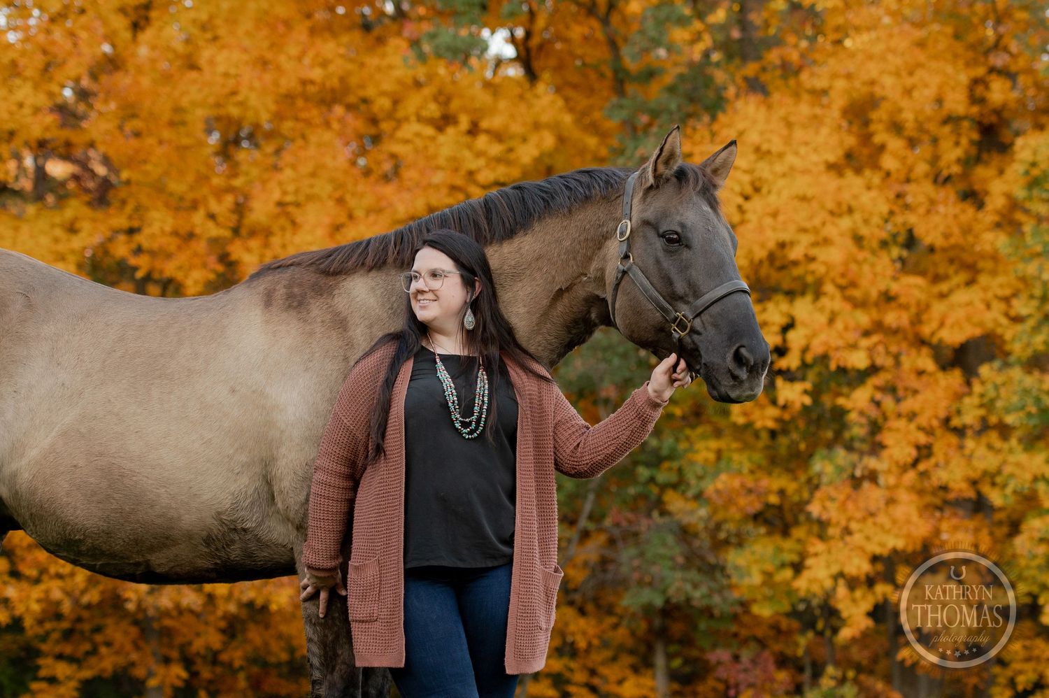 A gray horse stands majestically against bright orange autumn foliage during an outdoor photo session.