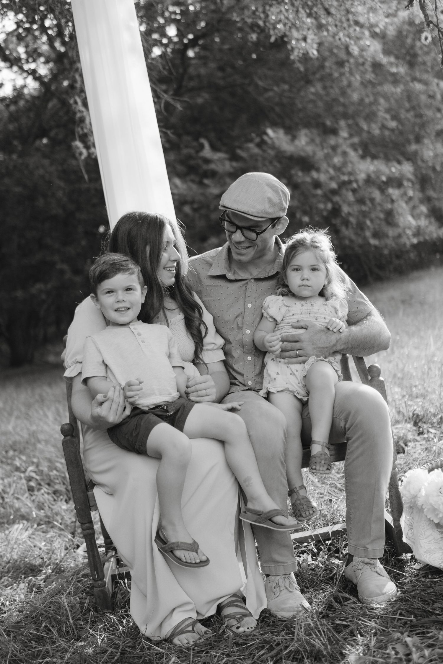 Black and white family portrait of parents and two young children sitting together outdoors on a bench.