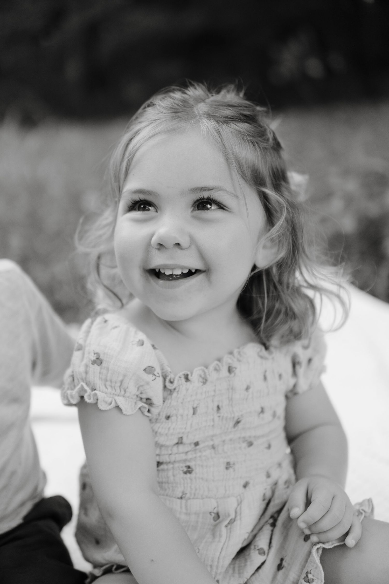 Black and white portrait of a smiling young child wearing a delicate lace dress with ruffled cap sleeves.