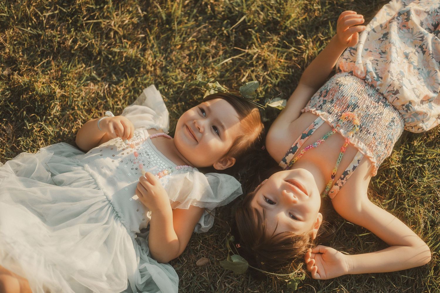 Two young people lying on grass in white dresses during golden hour.