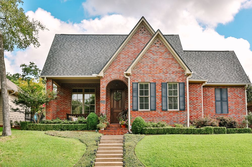 Traditional brick home with arched entryway and gray shutters on well-maintained lawn.