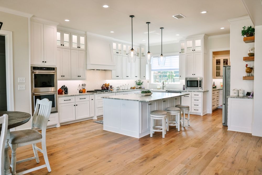 Bright modern white kitchen with hardwood floors, island, and pendant lighting.