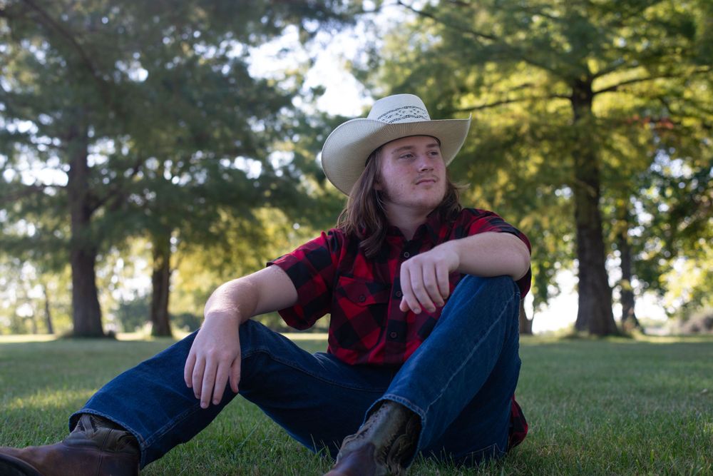Outdoor portrait in cowboy hat and plaid shirt against natural background.