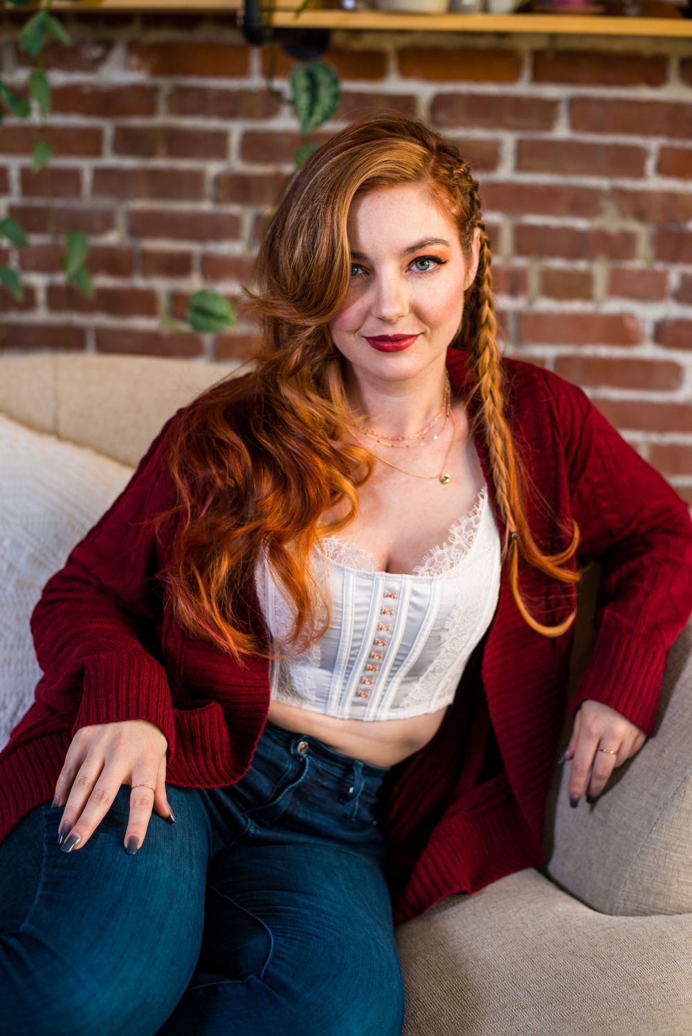 Cozy indoor portrait on grey sofa with burgundy sweater against brick wall.
