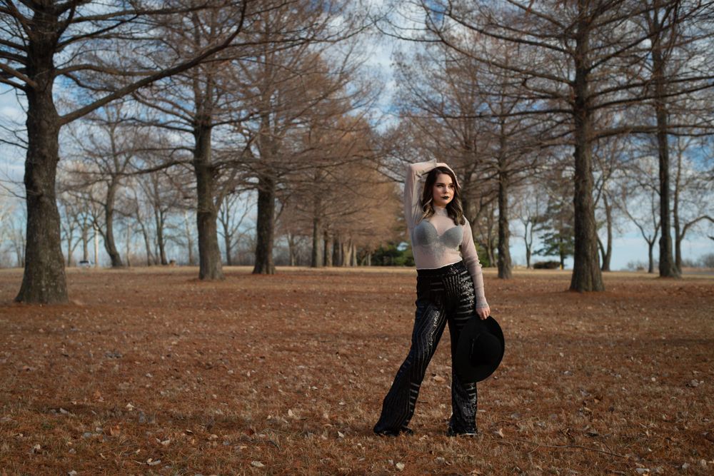 Person holding black balloons in autumn park with fallen leaves and bare trees.