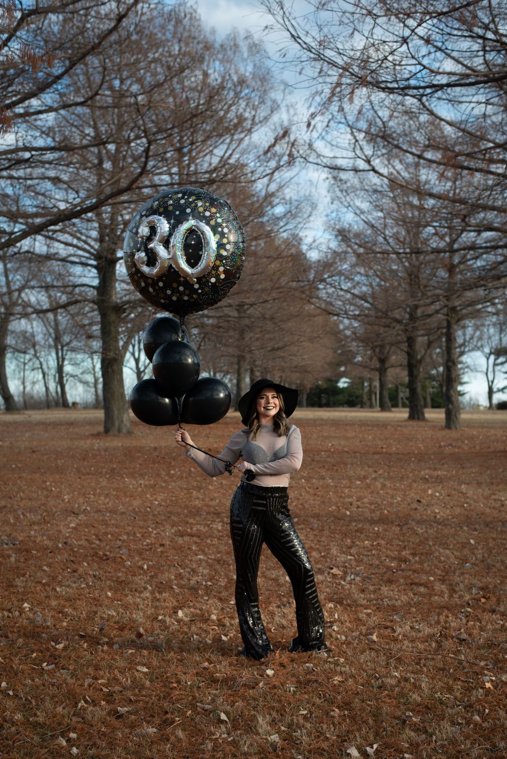 Black balloons floating against bare trees in autumn park setting.