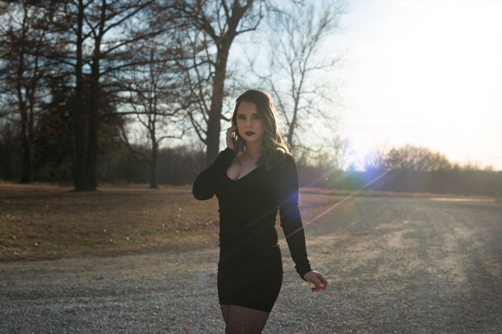 Silhouette walking through park at sunset with lens flare and bare trees.