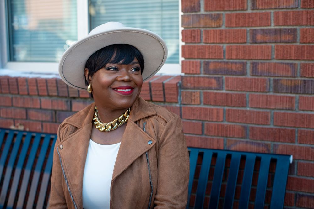 Outdoor portrait on bench against brick wall wearing tan hat.