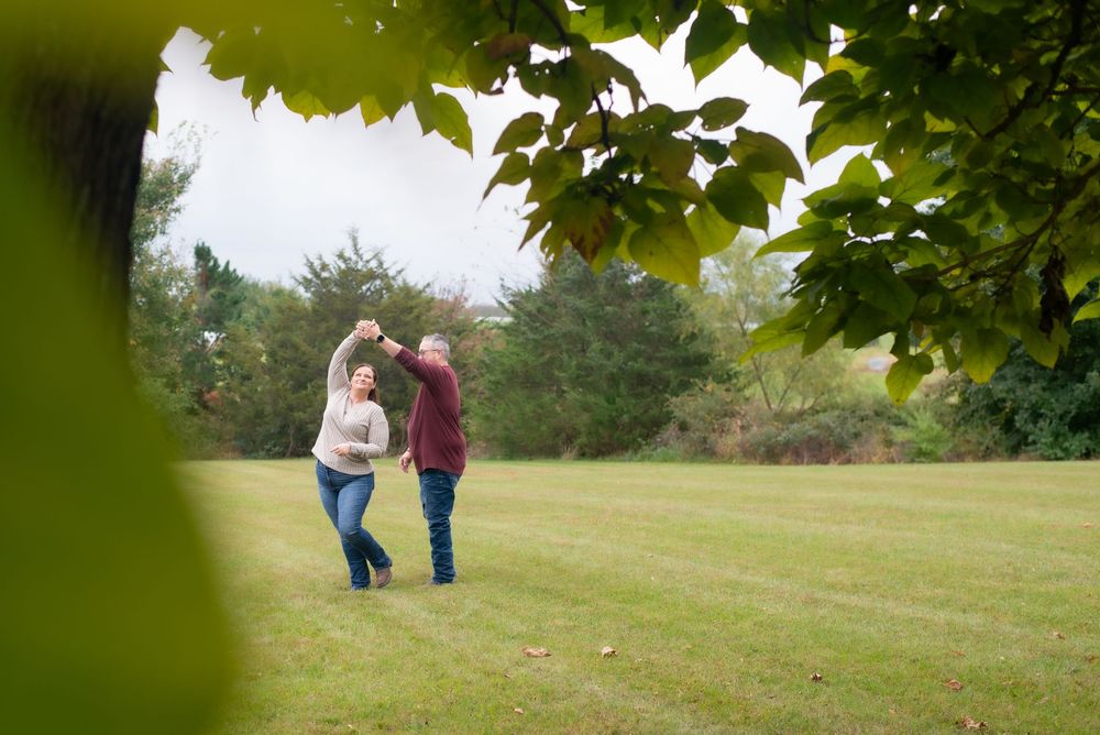 Distant view of couple walking together in a grassy field with trees.