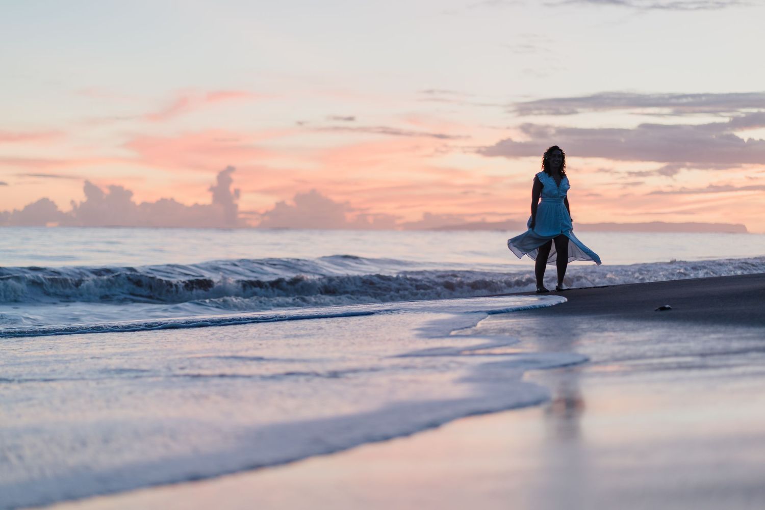 Silhouette of person walking on beach at sunset holding surfboard.