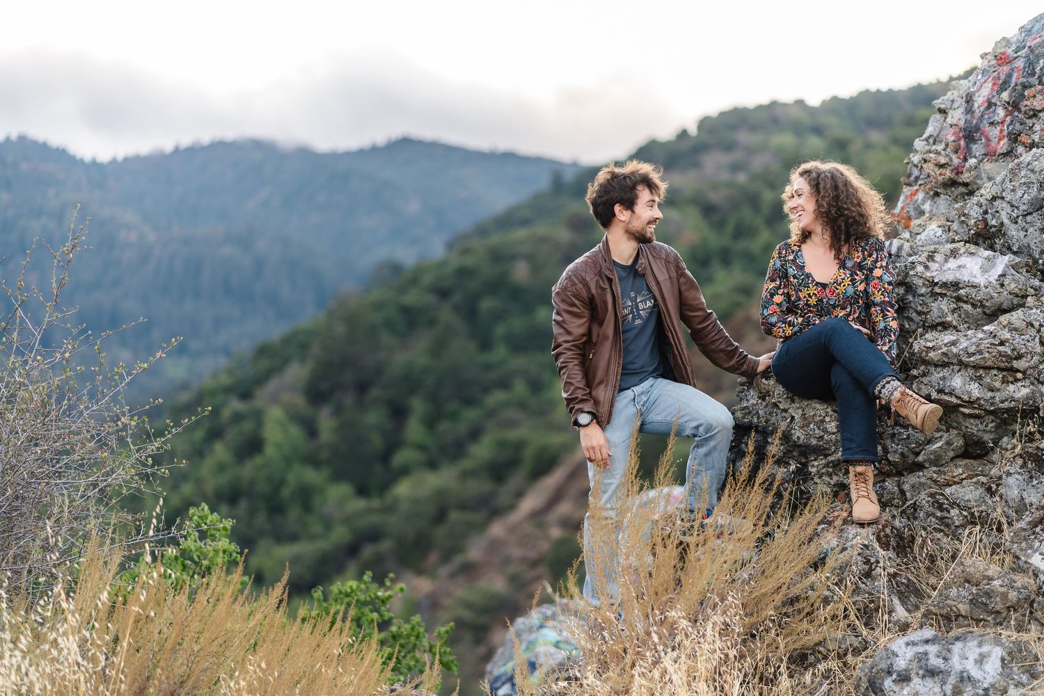 Couple sitting on rocky cliff edge having conversation with mountain vista behind them. Located near Felton.