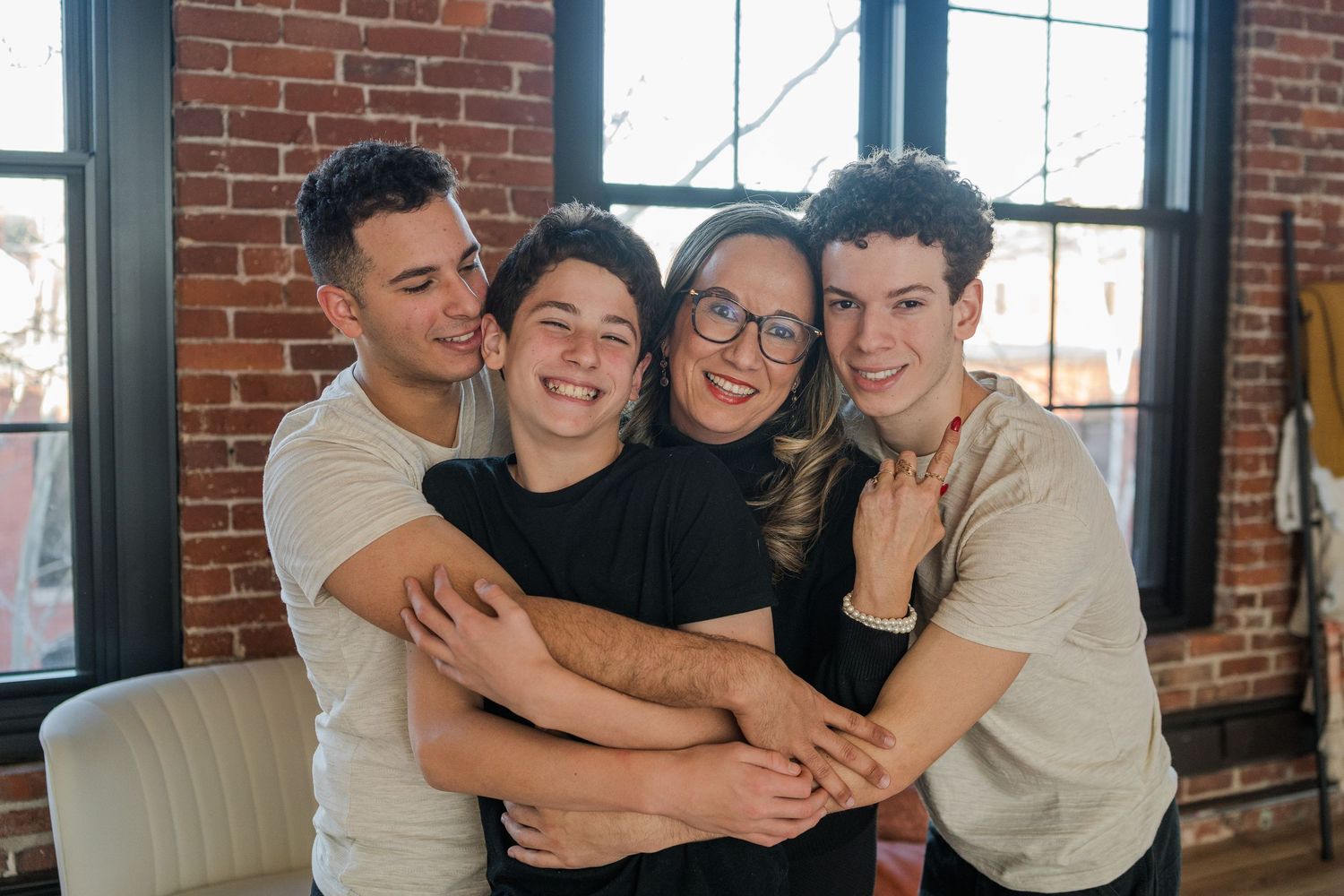 A group of people embrace in a warm group hug against a rustic brick wall background.