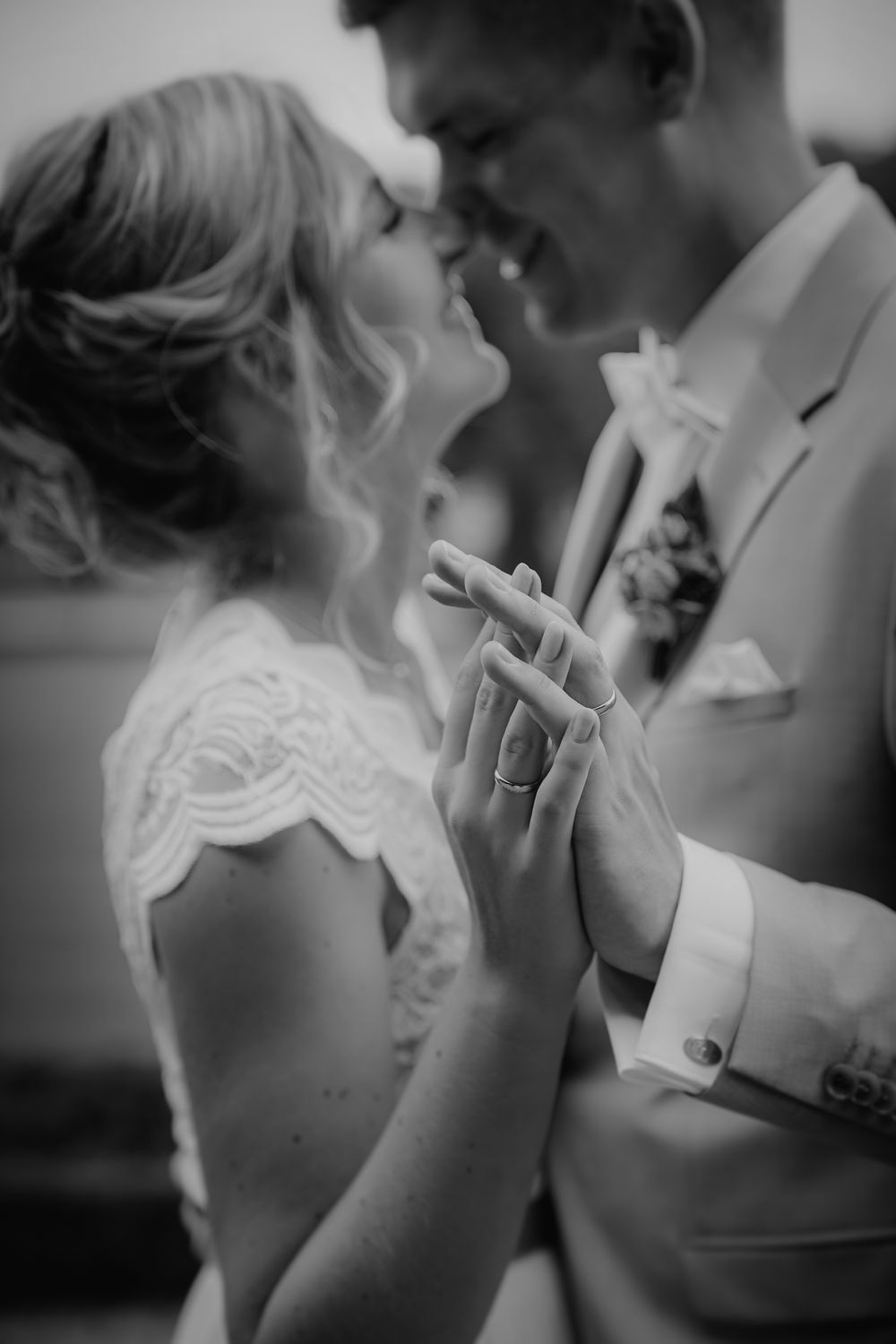 Romantic black and white wedding photo showing couple's hands clasped together with rings while sharing an intimate moment.
