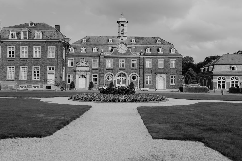 Stately historic mansion with symmetrical architecture and manicured gardens under cloudy sky.