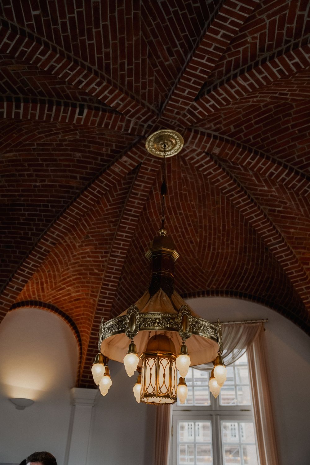 Ornate vintage chandelier hanging from decorative brick dome ceiling.