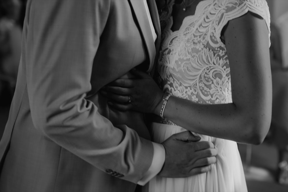 Intimate black and white photo of couple embracing, showing lace dress detail.
