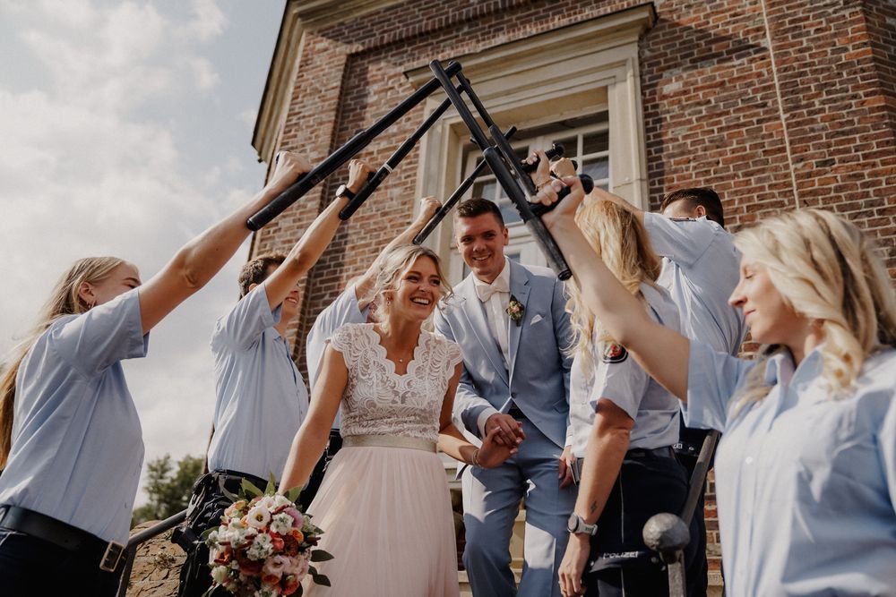Wedding party forming arch with raised arms for newlywed couple to walk through.