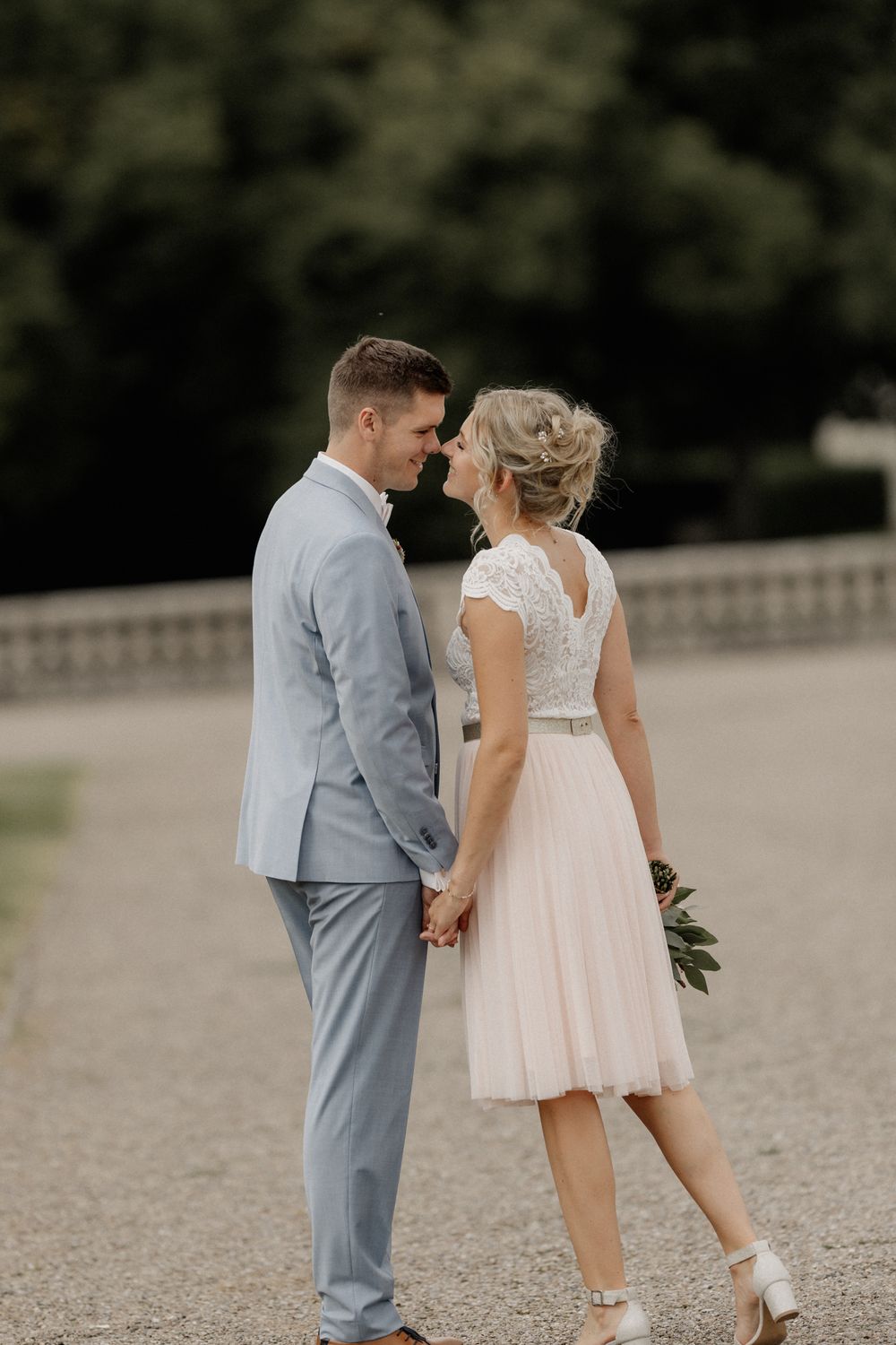 Romantic wedding couple in light attire walking together on gravel path.