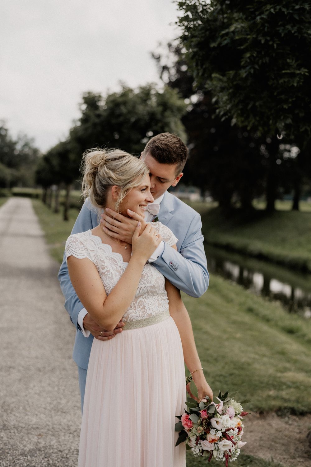Romantic wedding portrait on countryside path with couple embracing.