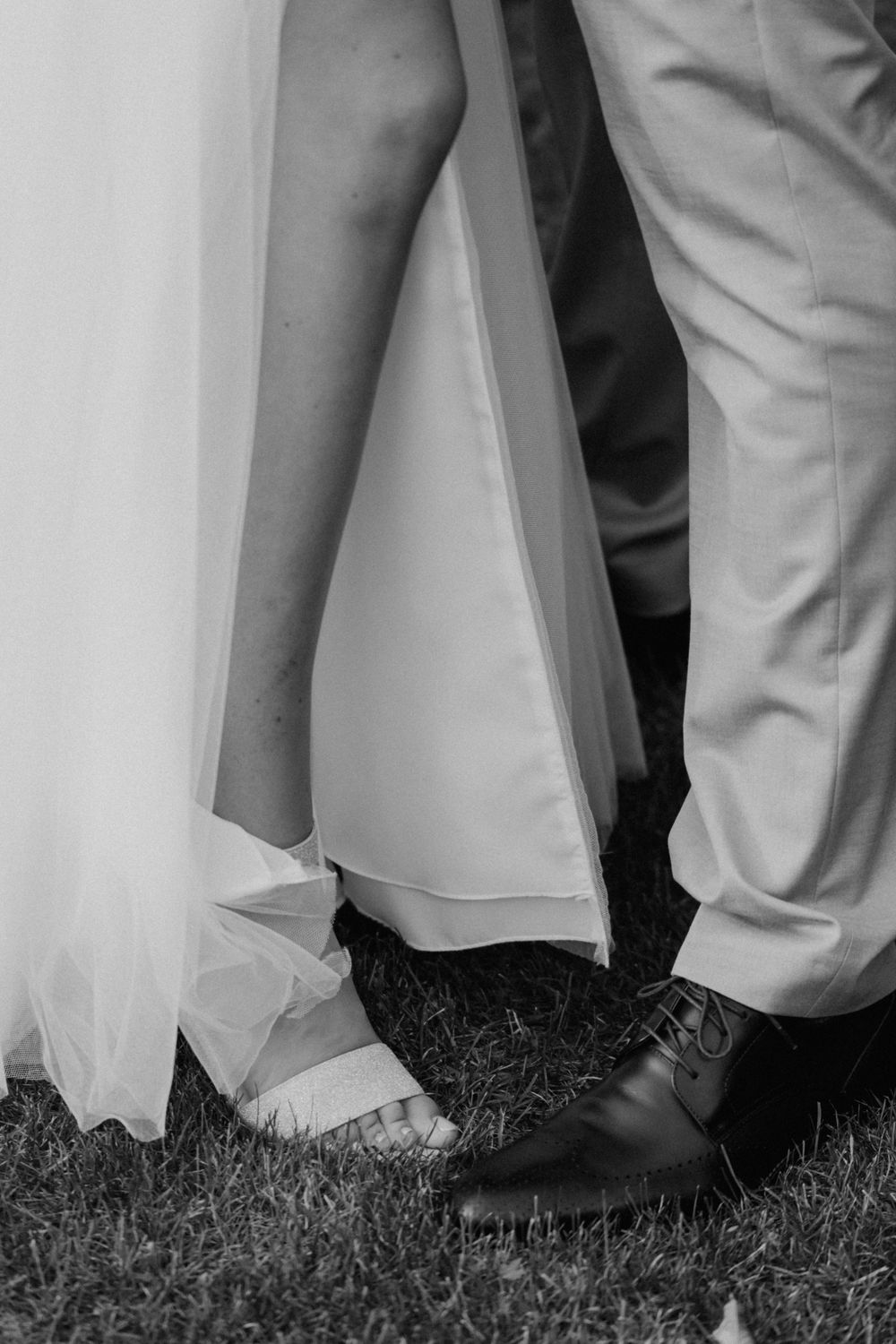 Black and white detail shot of bride and groom's feet standing together on grass.