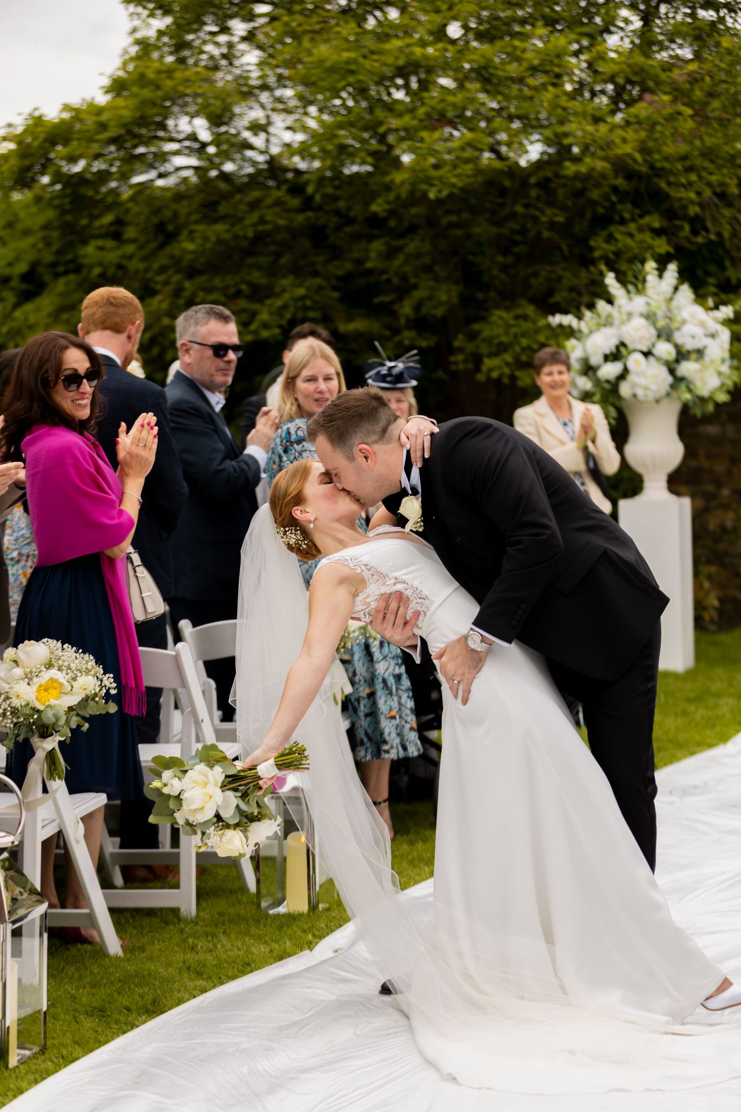 Wedding couple sharing romantic kisses during outdoor ceremony with white floral decorations.