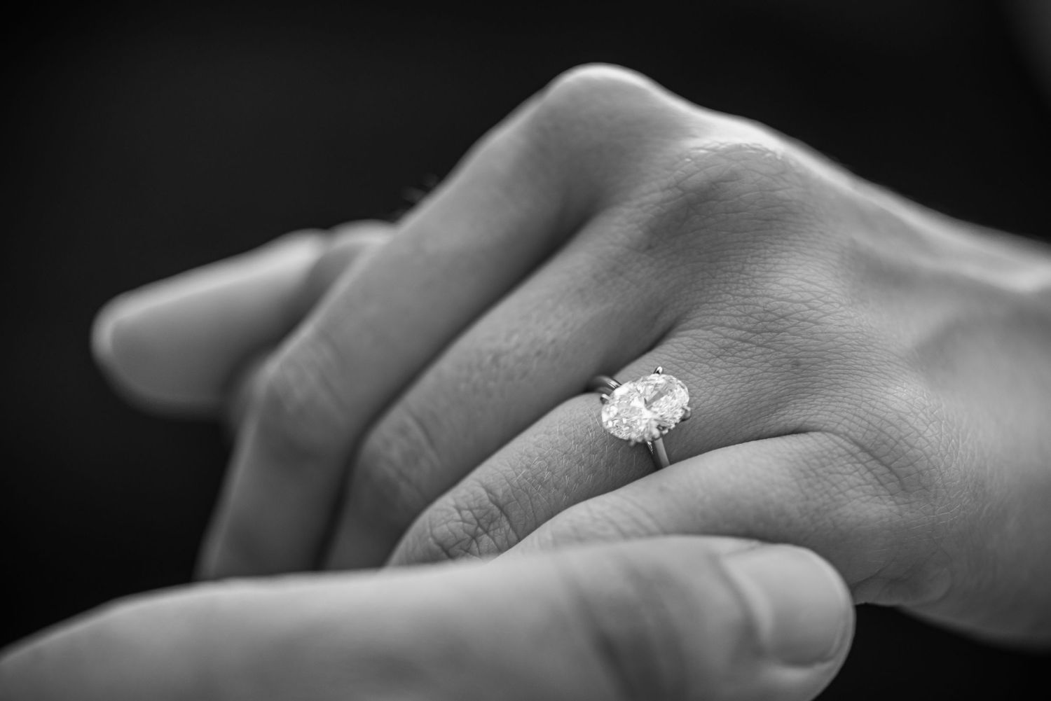 Close-up black and white photo of a sparkling diamond engagement ring on a hand.