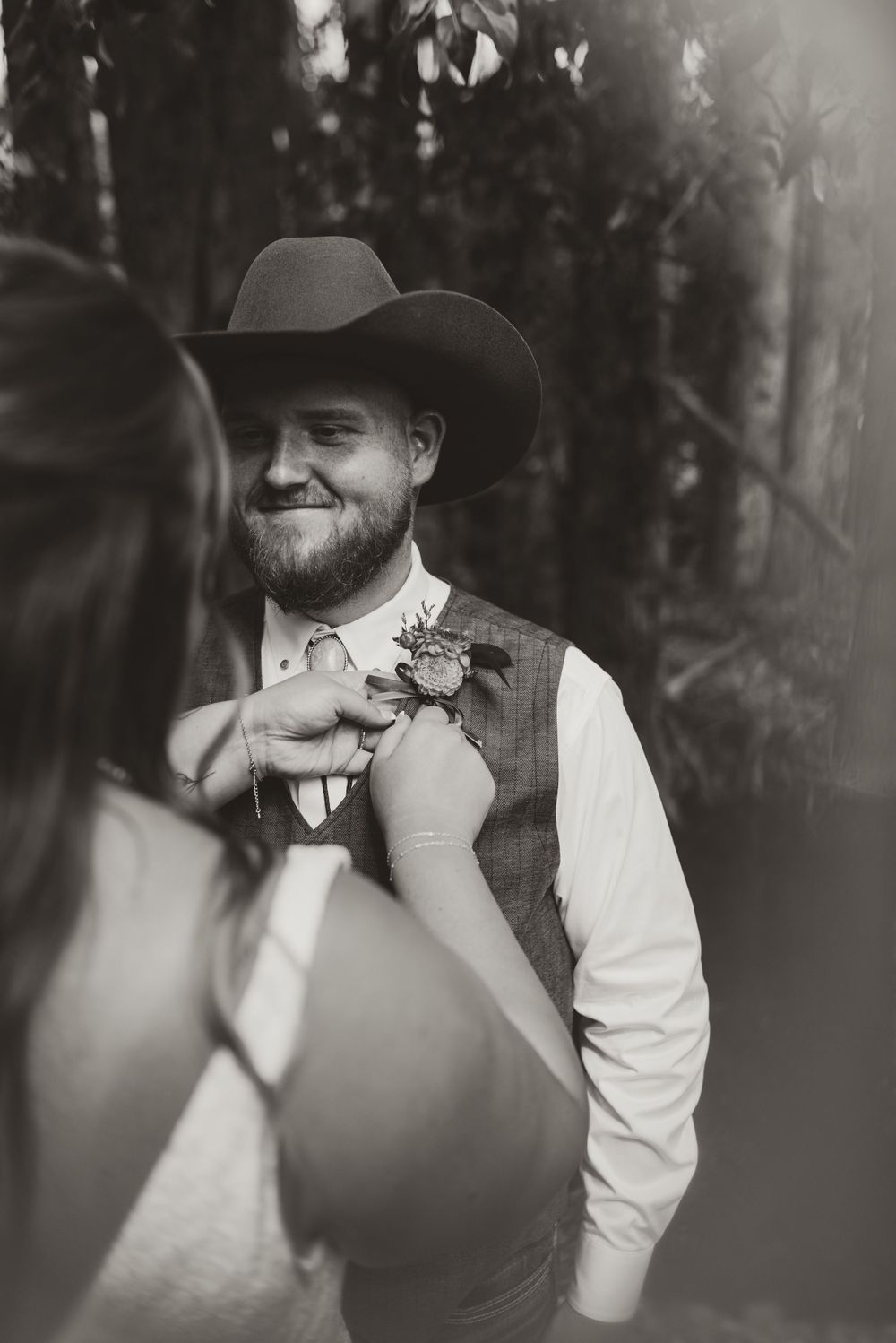 A boutonniere is being pinned on a grey vest during a western-themed wedding ceremony.