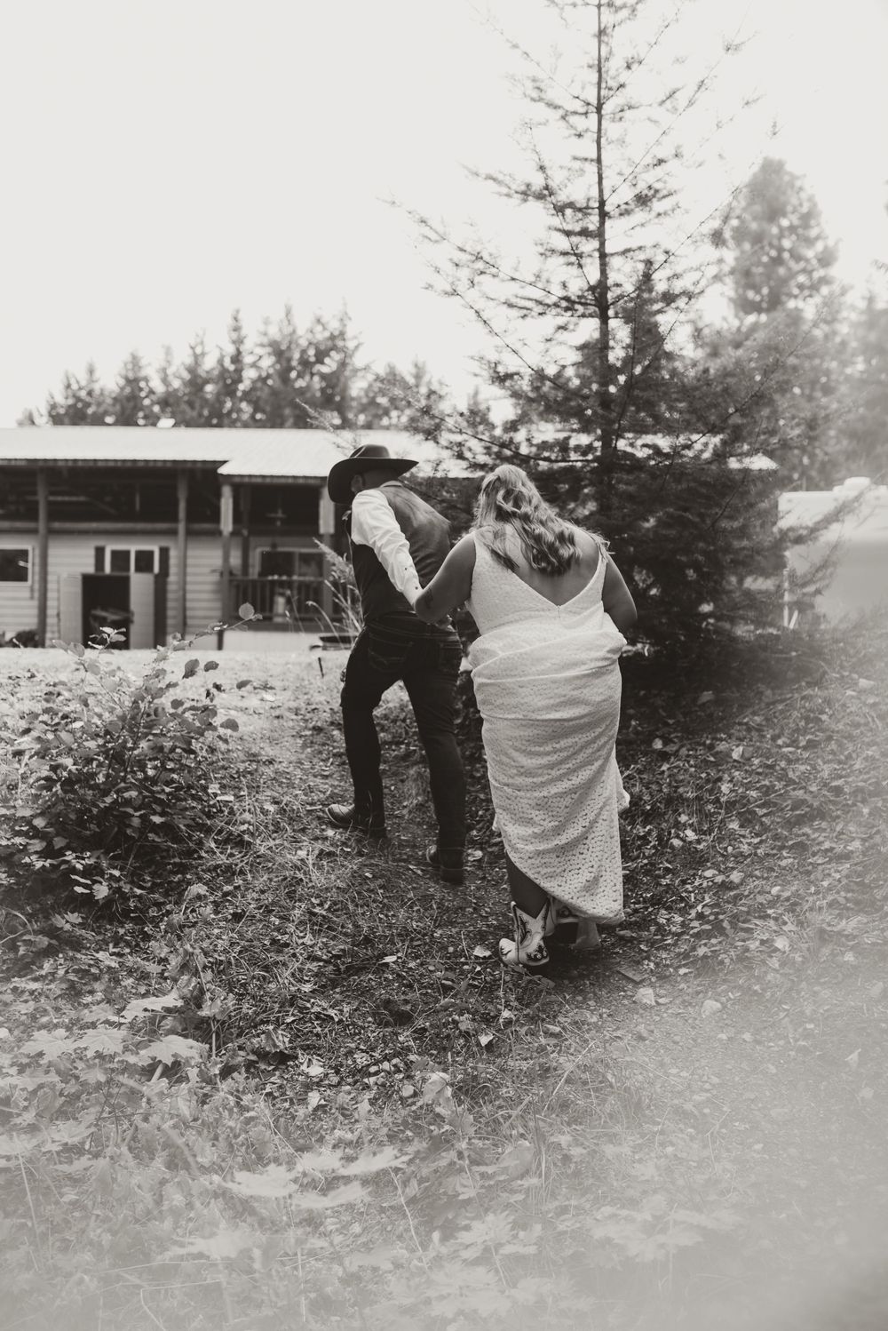 A vintage-style black and white photo of a couple dancing outdoors near a rustic building.