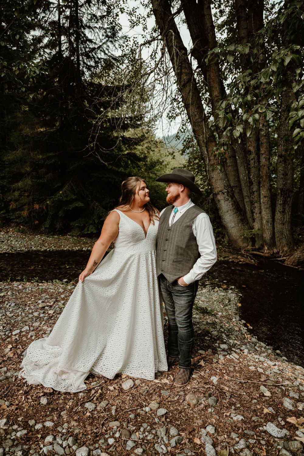 Newlyweds in rustic attire pose together on rocky forest path.