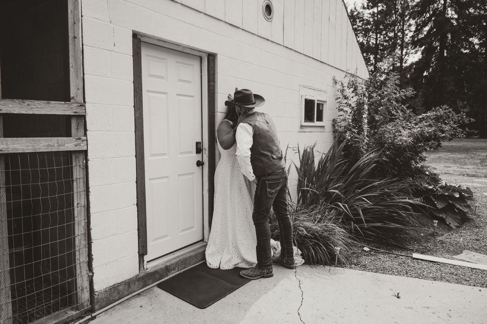 Black and white wedding photo of couple by white building entrance.