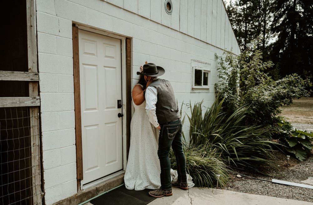 Intimate wedding portrait against white building with rustic landscape.